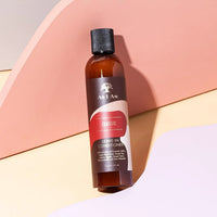 Braune Flasche As I Am Classic Leave-In Conditioner für lockiges und Afro-Haar vor pastellfarbenem Hintergrund